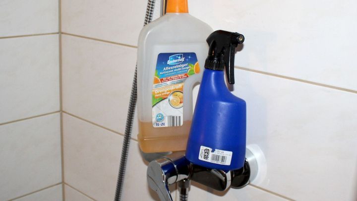 Eine blaue Spr&uuml;hflasche und eine transparente Flasche h&auml;ngen an einer Duschwand, bereit zur Reinigung der Badewanne und Duschtasse.