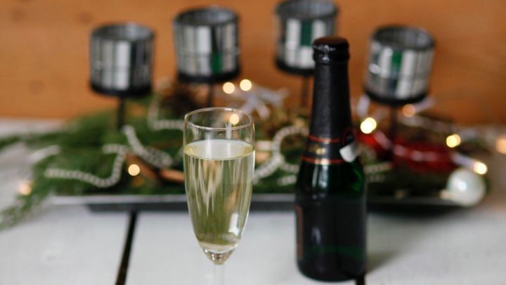 Ein Glas Champagner steht auf einem Tisch, w&auml;hrend eine Flasche Sekt daneben liegt, umgeben von festlicher Dekoration.