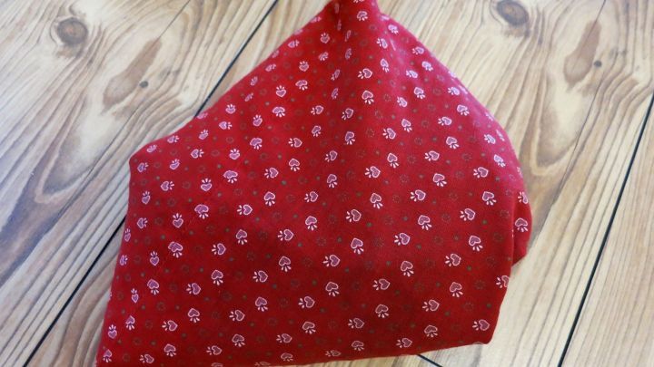 Ein Kirschkernsack liegt auf hellbraunem Holzfu&szlig;boden; er ist rot mit kleinen wei&szlig;en Mustern bedruckt.