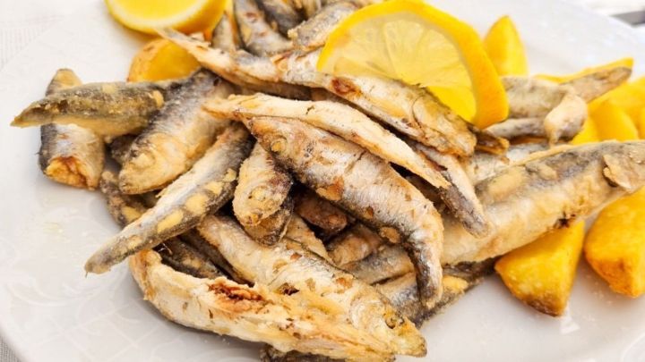 Gebratene Fische liegen auf einem Teller, garniert mit Zitronenscheiben und umgeben von knusprigen Pommes Frites.