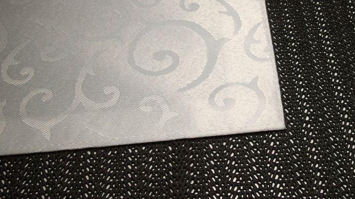 Eine glatte, wei&szlig;e Oberfl&auml;che mit dezentem Muster liegt auf einem dunklen, strukturierten Hintergrund.