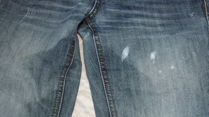 Jeans mit Farbspritzern auf der Vorderseite liegen auf einer hellen Oberfl&auml;che, die Abnutzungsspuren zeigt.
