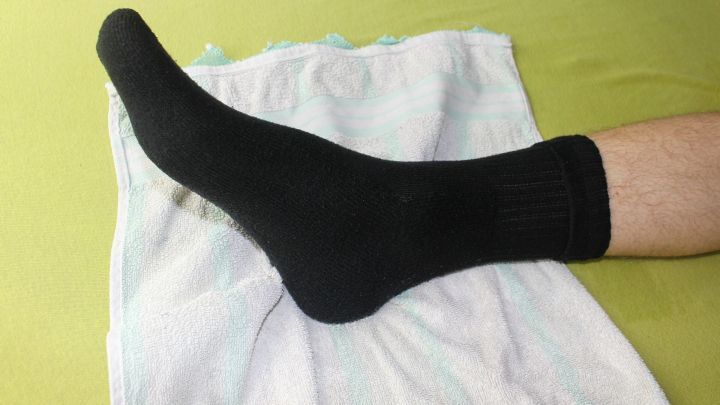 Ein nasser Baumwollsocken liegt auf einem Handtuch, w&auml;hrend ein Fu&szlig; den Socken anzieht, um bei Hitze zu schlafen.