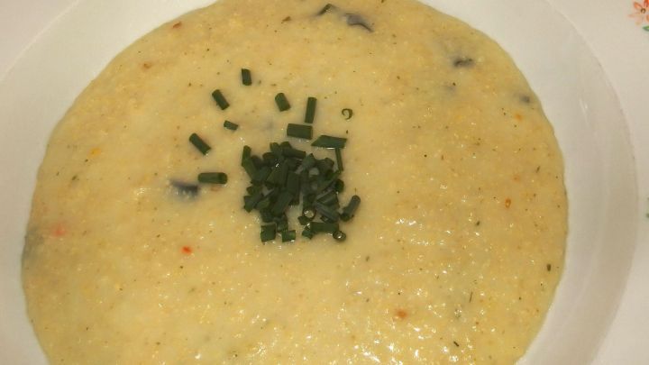 Eine cremige Hirsesuppe liegt in einer Schale, garniert mit frischem Schnittlauch in einer einfachen K&uuml;chenszene.