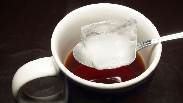 Eine Tasse mit Tee und einem Eisw&uuml;rfel darin, der schmelzend die Temperatur des Getr&auml;nks senkt.