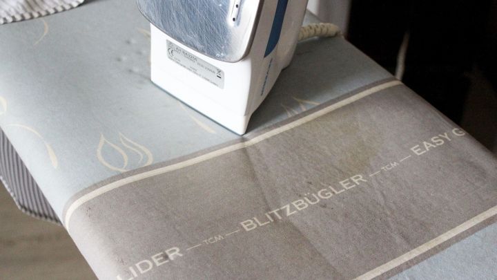 Ein B&uuml;geleisen gleitet &uuml;ber einen Blitzb&uuml;gel-Bezug auf einem B&uuml;gelbrett in einer hellen Umgebung und gl&auml;ttet Stoffe.