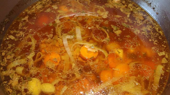 Ein Wurzeltopf k&ouml;chelt in einem Topf mit einer bunten Mischung aus Gem&uuml;se und Gew&uuml;rzen in einer Br&uuml;he.