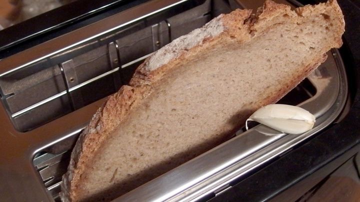 Ein St&uuml;ck Vollkornbrot wird im Toaster ger&ouml;stet, w&auml;hrend eine Knoblauchzehe daneben liegt, bereit zum Aufstrich.