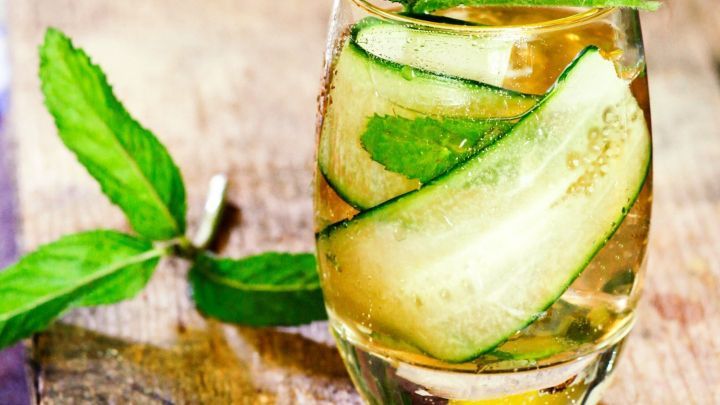 Ein Glas Gurkenbowle steht auf einer Holzoberfl&auml;che. Frische Gurkenscheiben und Minze schwimmen im Getr&auml;nk.