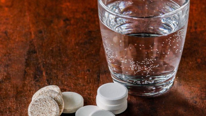 Sprudeltabletten liegen neben einem Glas Wasser, das auf einem Holztisch steht, um bei Kater Magnesium zu liefern.