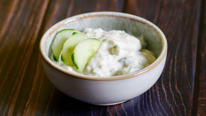 Ein Sch&auml;lchen mit selbstgemachtem Tsatsiki, garniert mit Gurkenscheiben, steht auf einem rustikalen Holztisch.
