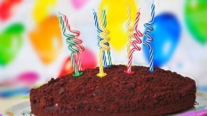 Der Maulwurfkuchen steht auf einem Teller mit bunten, spiralf&ouml;rmigen Kerzen. Im Hintergrund sind verschwommene Luftballons sichtbar.