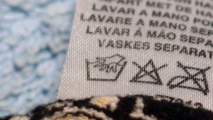 Ein Pflegeetikett zeigt Anweisungen zur Handw&auml;sche mit Haarshampoo auf einem bunten Stoffrest, umgeben von einem blauen Tuch.