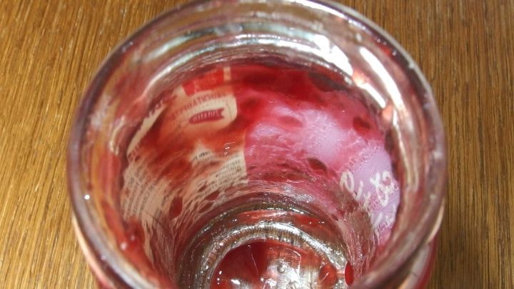 Ein Glas mit Marmelade zeigt Reste am Boden und an den Seiten, w&auml;hrend es auf einer Holzoberfl&auml;che steht.