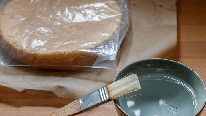Ein Tortenboden liegt in einem Plastikbeutel, daneben steht eine Sch&uuml;ssel mit Wasser und einem Pinsel.