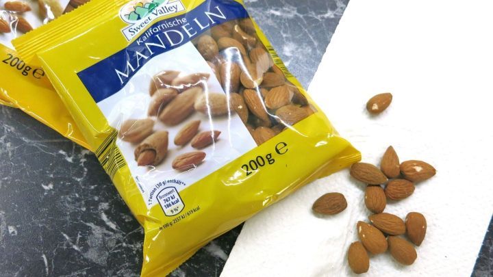 T&uuml;ten mit Mandeln liegen neben einer offenen Packung, aus der einige Mandeln auf ein Papiertuch gefallen sind.
