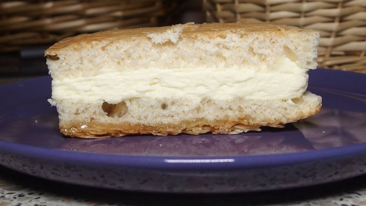 Ein St&uuml;ck Bienenstich liegt auf einem blauen Teller und zeigt die helle F&uuml;llung zwischen den Teigschichten.