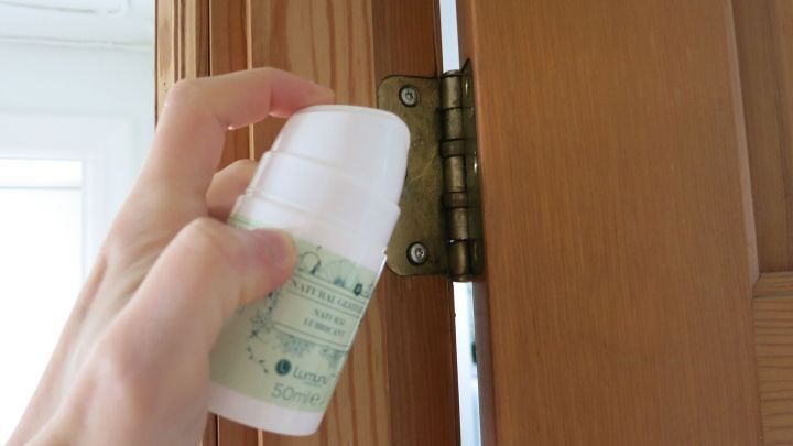 Eine Hand h&auml;lt eine Flasche Gleitgel, w&auml;hrend sie es auf ein T&uuml;rscharnier auftr&auml;gt, um es zu schmieren.