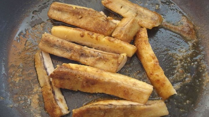 In einer Pfanne braten gebratene Curry-Bananen in goldbrauner Farbe, umgeben von einer leicht &ouml;ligen Oberfl&auml;che.