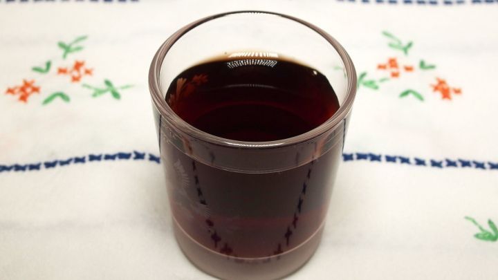 Ein Glas Pflaumenlik&ouml;r steht auf einem gemusterten Tischset, umgeben von floralen Motiven auf dem Stoff.