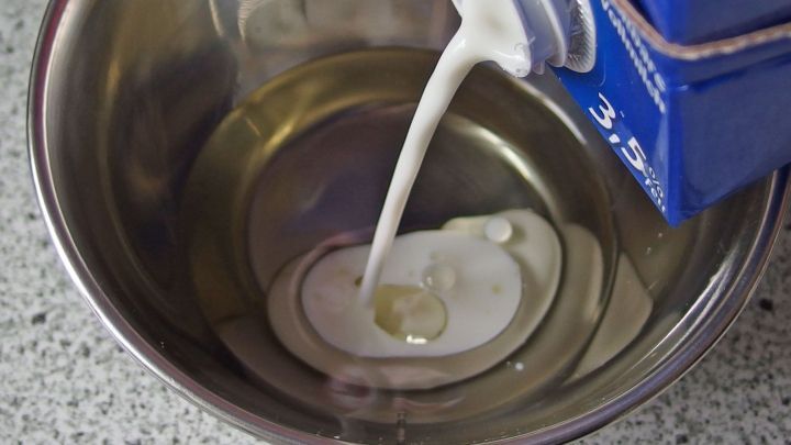 Eine Fl&uuml;ssigkeit, vermutlich Milch, wird in eine Sch&uuml;ssel mit Oliven&ouml;l gegossen, auf einer K&uuml;chenoberfl&auml;che.