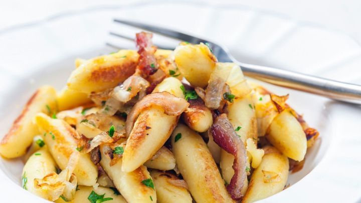 Saftige Schupfnudeln werden mit knusprigem Schinken und Zwiebeln auf einem wei&szlig;en Teller serviert.