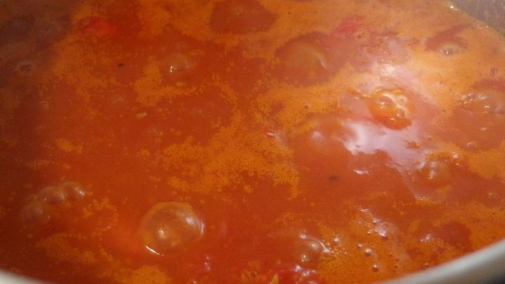 Eine Tomatensauce k&ouml;chelt in einem Topf, der von dampfendem, aromatischem Inhalt umgeben ist.