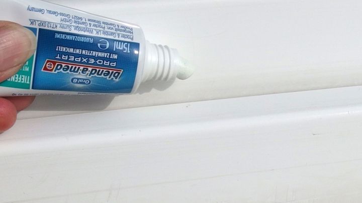 Eine Hand h&auml;lt eine Tube Zahncreme, die auf einen wei&szlig;en Fensterrahmen aufgetragen wird, um ihn zu reinigen.