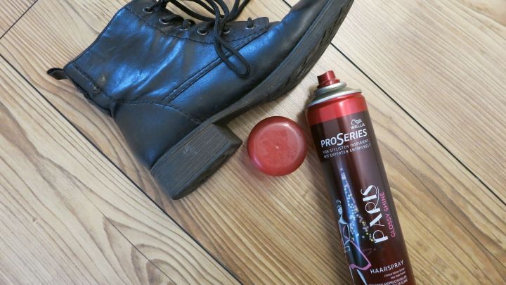 Ein schwarzer Lederschuh liegt auf einem Holzboden neben einer Dose Haarspray, bereit f&uuml;r schnellen Schuhglanz.