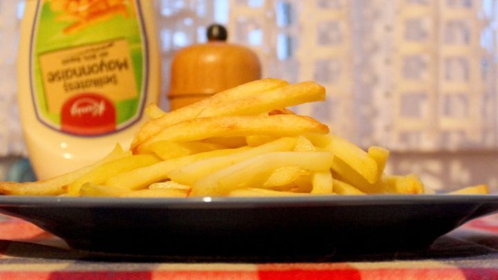 Eine Portion Pommes Frites liegt auf einem Teller, umgeben von einem Ketchupbeh&auml;lter und einer Gew&uuml;rzm&uuml;hle in einer gem&uuml;tlichen K&uuml;che.