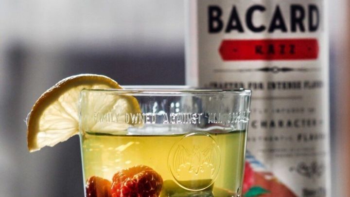 Ein Glas mit einem erfrischenden Ginger-Razz-Cocktail steht auf einem Tisch, umgeben von einer Bacardi-Flasche.