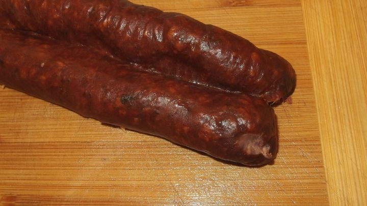 Dunkle Knackwurst und Mettwurst liegen auf einem Holzbrett, bereit zum Entfernen der Pelle f&uuml;r die Zubereitung.