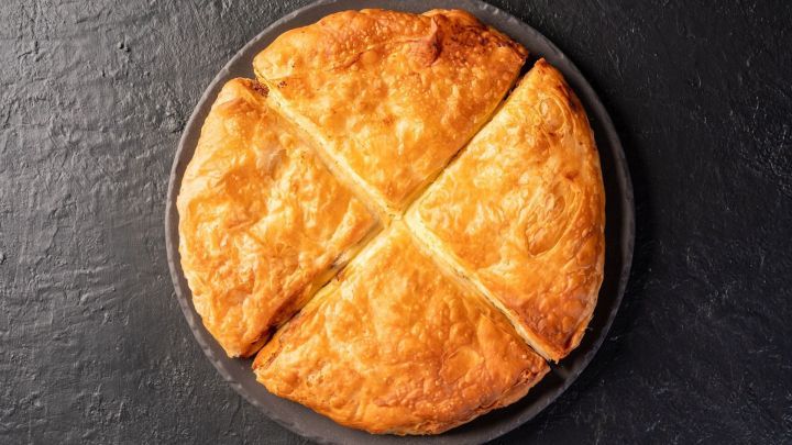 Ein goldbrauner Kartoffelkuchen liegt auf einer dunklen Platte, in vier gleichm&auml;&szlig;ige St&uuml;cke geschnitten.