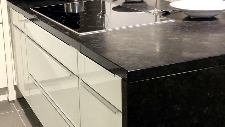 Eine moderne K&uuml;chenarbeitsplatte aus Stein, auf der ein Topf kocht, steht in einer stilvollen, hellen K&uuml;che.