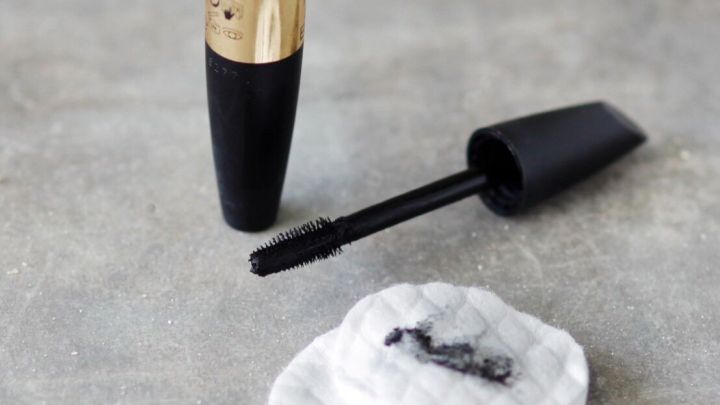 Ein schwarzer Mascara-Stift liegt offen neben einem verschmutzten, wei&szlig;en Wattepad auf einer hellen Oberfl&auml;che.
