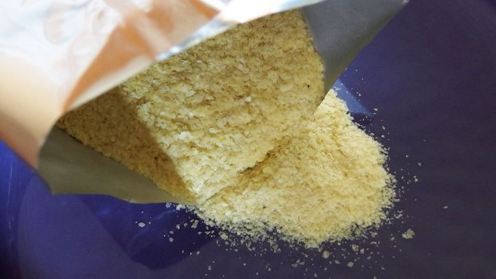 Ein P&auml;ckchen Kartoffelp&uuml;reepulver wird auf einen blauen Teller gesch&uuml;ttet, um eine Suppe oder Sauce zu verdicken.