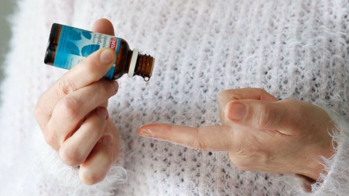 Eine Person h&auml;lt eine Flasche Minz&ouml;l und gibt einen Tropfen auf ihren Finger, um damit die Schnupfennase zu lindern.