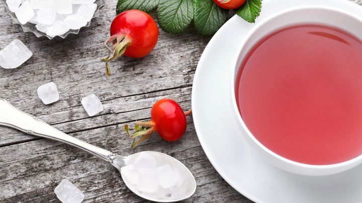 Hagebuttentee in einer Tasse wird mit Zucker und frischen Hagebutten auf einem rustikalen Holztisch serviert.