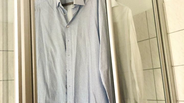 Im Badezimmer h&auml;ngen ein blauer Hemd und ein wei&szlig;es Hemd zum Trocknen an einer Stange in einer Dusche.