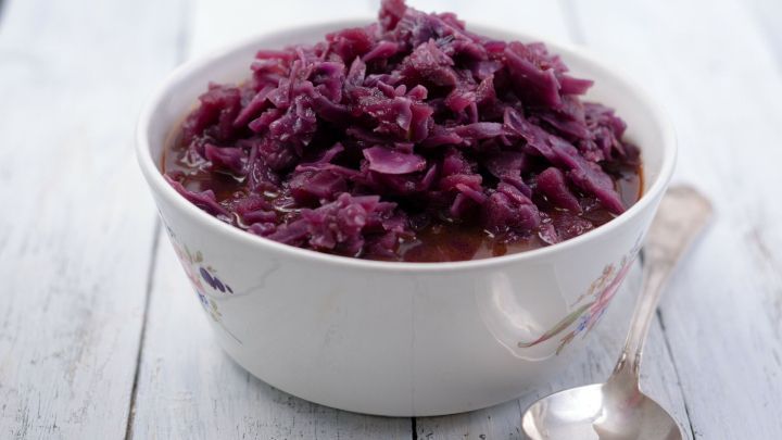 In einer dekorativen Sch&uuml;ssel liegt frisch zubereiteter Rotkohl in einer aromatischen Br&uuml;he, auf einem hellen Holzuntergrund.
