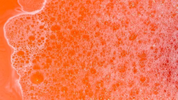 Oranges, sch&auml;umendes Badewasser sprudelt, bedeckt mit vielen kleinen Blasen, und f&uuml;llt einen bunten Badebereich aus.