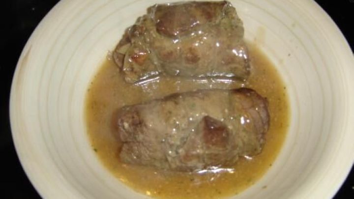 Zwei geschmorte Rinderrouladen liegen in einer herzhaften So&szlig;e auf einem wei&szlig;en Teller.