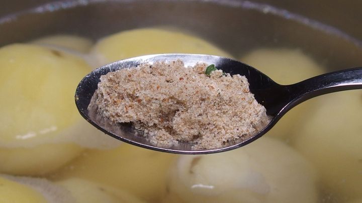 Eine L&ouml;ffel mit Gew&uuml;rzen schwebt &uuml;ber einem Topf mit gekochten Salzkartoffeln, bereit zum Aufpeppen des Gerichts.