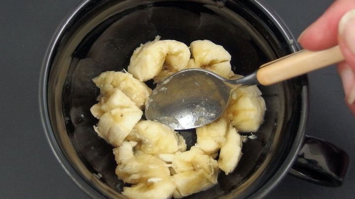 Eine Hand benutzt einen L&ouml;ffel, um zerdr&uuml;ckte Bananen in einer schwarzen Tasse zu vermischen. Kein Ei im Haus zum Kuchen backen?