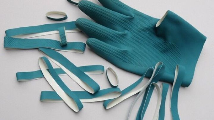 Ein abgenutzter, blauer Gummihandschuh liegt mit zerrissenen Gummi&uuml;berresten auf einer wei&szlig;en Fl&auml;che, bereit zur Wiederverwertung.