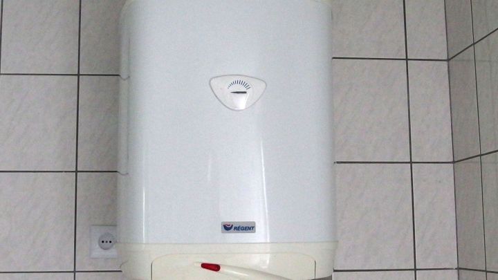 Ein elektrischer Durchlauferhitzer h&auml;ngt an einer gefliesten Wand, bereit dazu, Wasser zu erw&auml;rmen und Energie zu sparen.