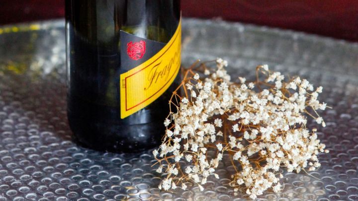 Eine Weinflasche steht auf einem metallenen Untergrund, umgeben von kleinen bl&uuml;henden Pflanzen, die ein bezauberndes Ambiente schaffen.