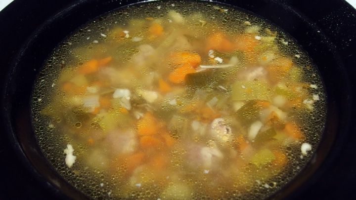 Eine dampfende Br&uuml;he befindet sich in einer schwarzen Schale, umgeben von buntem Gem&uuml;se, ideal gegen Kater.