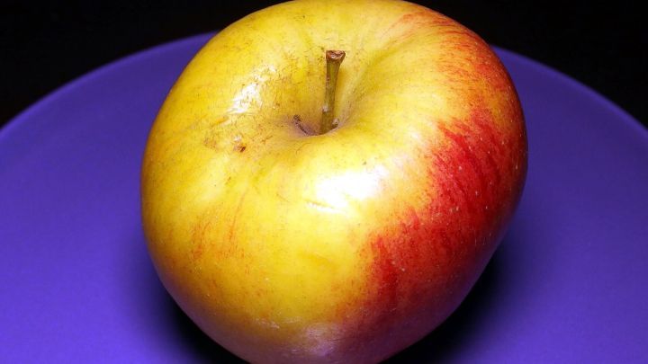 Ein roter Apfel liegt auf einem lila Teller vor einem dunklen Hintergrund, bereit zum Genie&szlig;en f&uuml;r Kinder, die Obstmuffel sind.