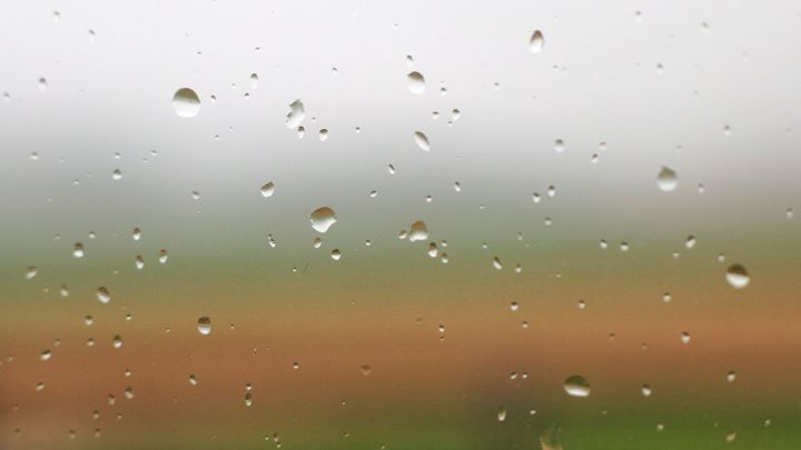 Wassertropfen haften an einem Fenster, w&auml;hrend der Hintergrund unscharf und gr&uuml;nlich erscheint, ideal f&uuml;r Fensterputzen.